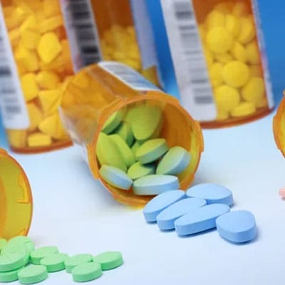 Prescription bottles with yellow, green, and blue pills scattered on a white surface.